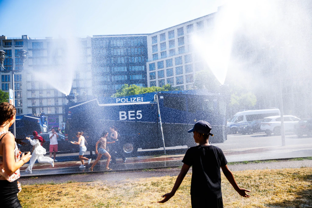 Passanten stehen vor einem Wasserwerfer der Polizei. Die Polizei sprüht Wasser zur Abkühlung für die Menschen am Potsdamer Platz.