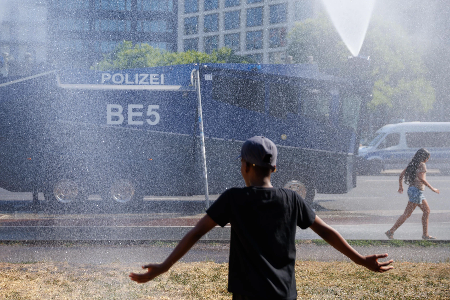 Menschen stehen am Potsdamer Platz vor einem Wasserwerfer der Polizei, der Wasser zur Abkühlung spritzt.