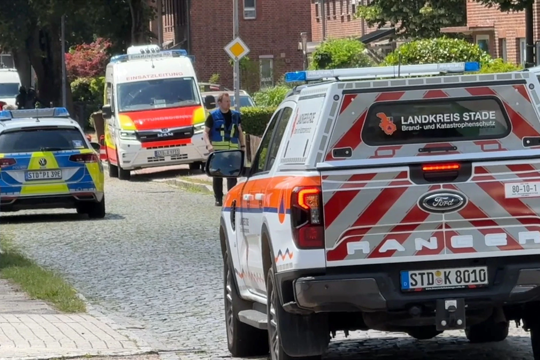 Einsatzkräfte stehen auf einer Straße in Stade. In einer Jugendhilfeeinrichtung sind sechs Menschen getötet worden.