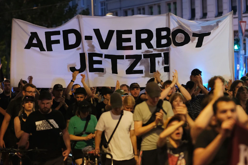 Teilnehmer einer linken Demonstration gehen mit Transparent mit der Aufschrift «AfD- Verbot jetzt!» eine Straße entlang.