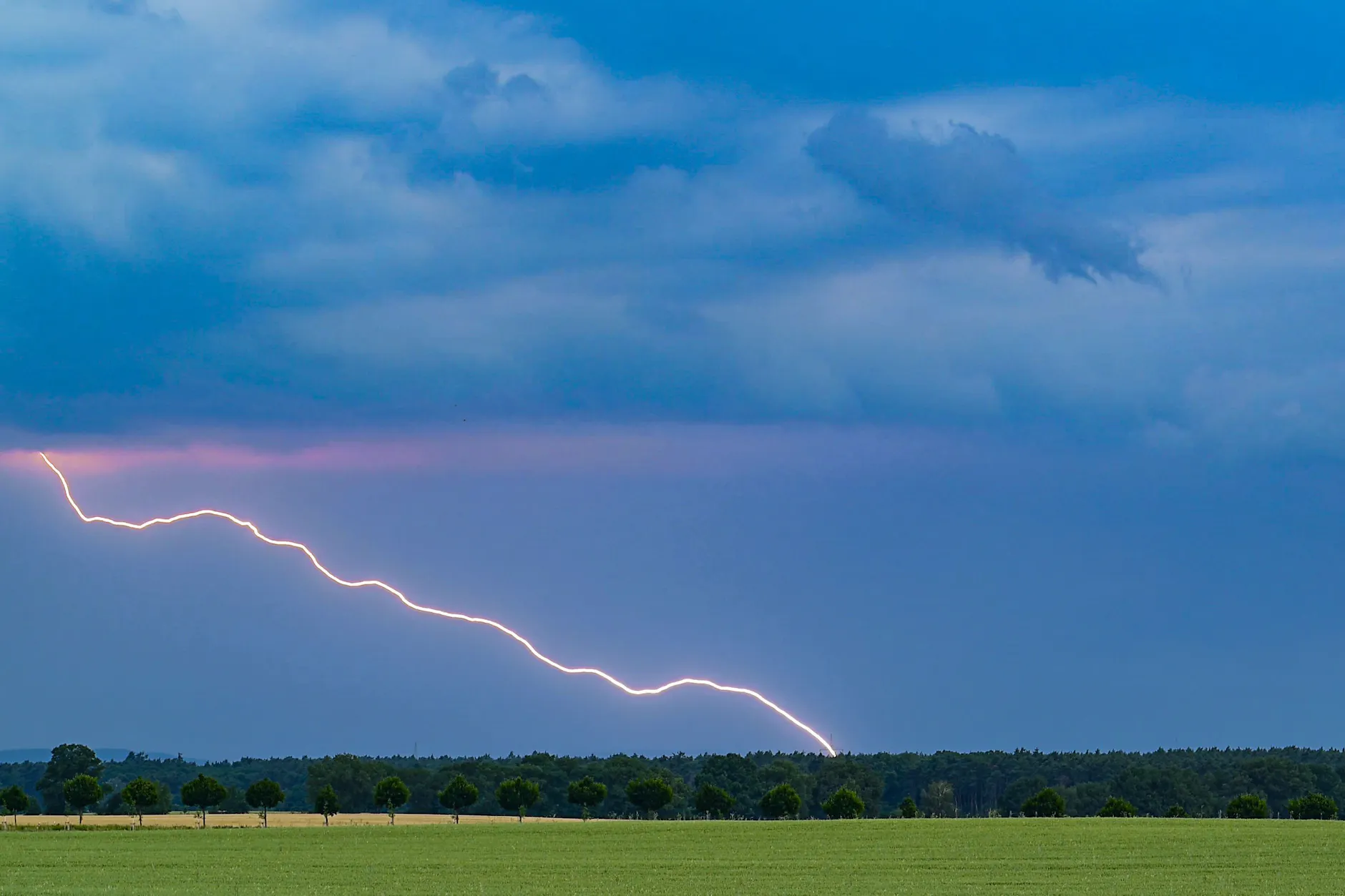 Ein Blitz leuchtet vor dunklen Gewitterwolken über der Landschaft im östlichen Brandenburg.