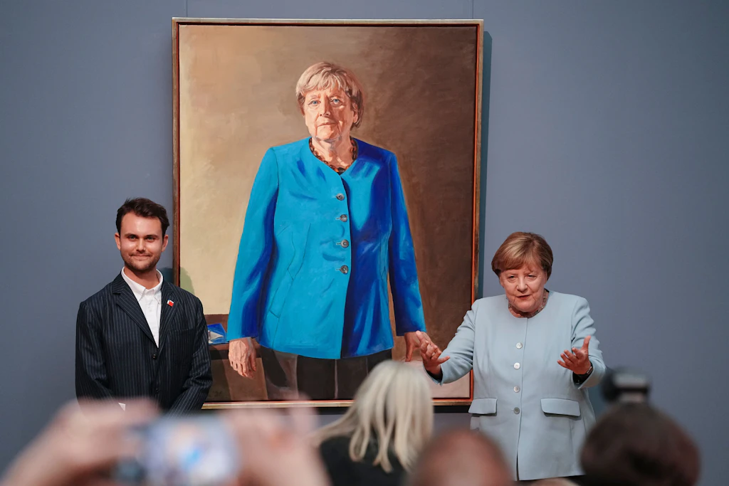 Sehr blau, sehr maskulin: das Porträt der Altkanzlerin. Neben Merkel links: der junge Künstler Jérémie Queyras.
