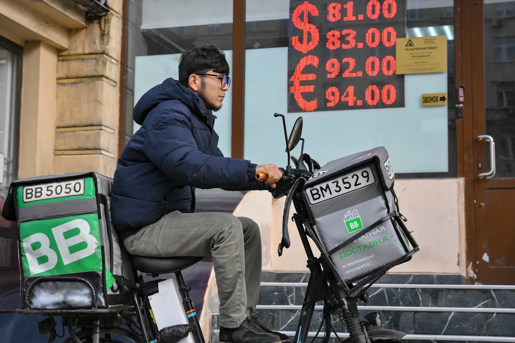 Ein Lieferbote fährt an einer Tafel mit Wechselkursen für den Dollar und den Euro gegenüber dem Rubel in Moskau vorbei.