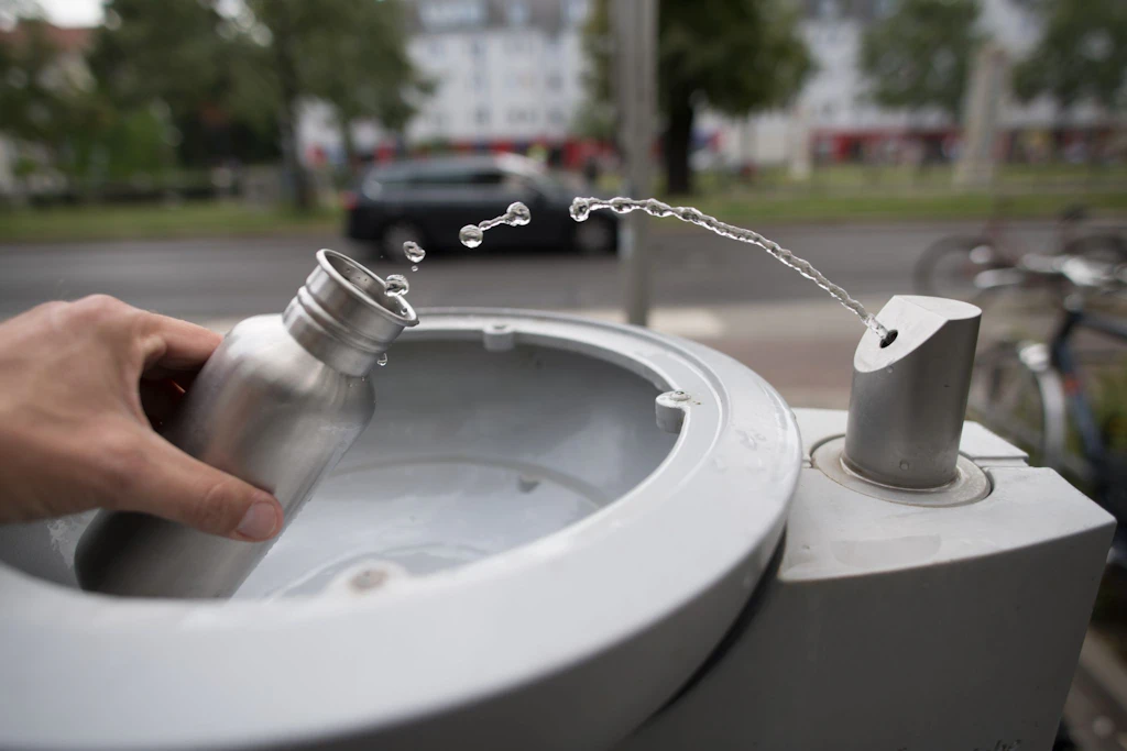 An einem Wasserspender füllt ein Passant seine Trinkflasche mit Wasser auf.