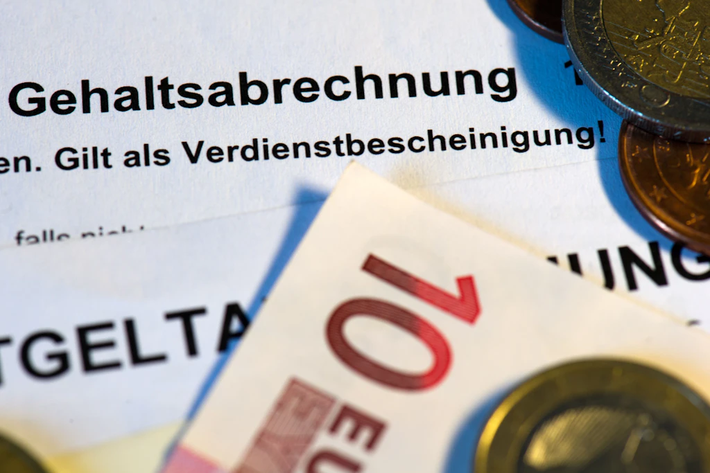 Eine Gehaltsabrechnung mit Euromünzen. Für Gutverdiener könnten die Sozialabgaben im Jahr 2027 deutlich steigen.