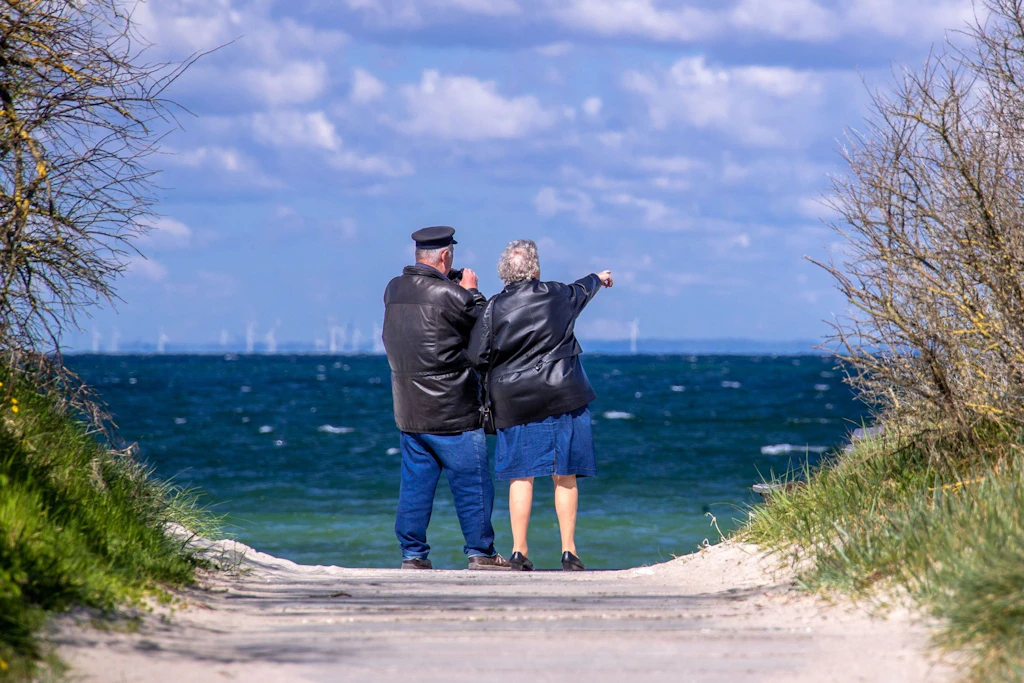 Ein Rentnerpaar steht am ansonsten menschenleeren Strand und schaut aufs Meer.