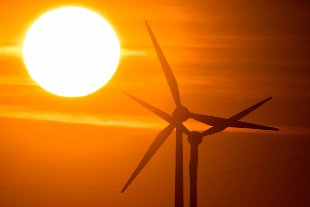 Die Sonne geht hinter Windrädern auf. (Symbolbild)