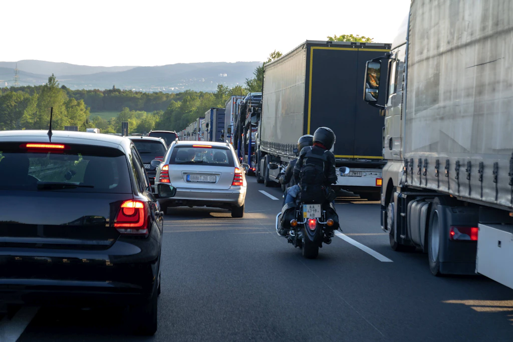 Stau auf der Autobahn: Zahlreiche Lkw und Pkw stehen dicht an dicht, während ein Motorradfahrer sich zwischen den Fahrzeugen bewegt.