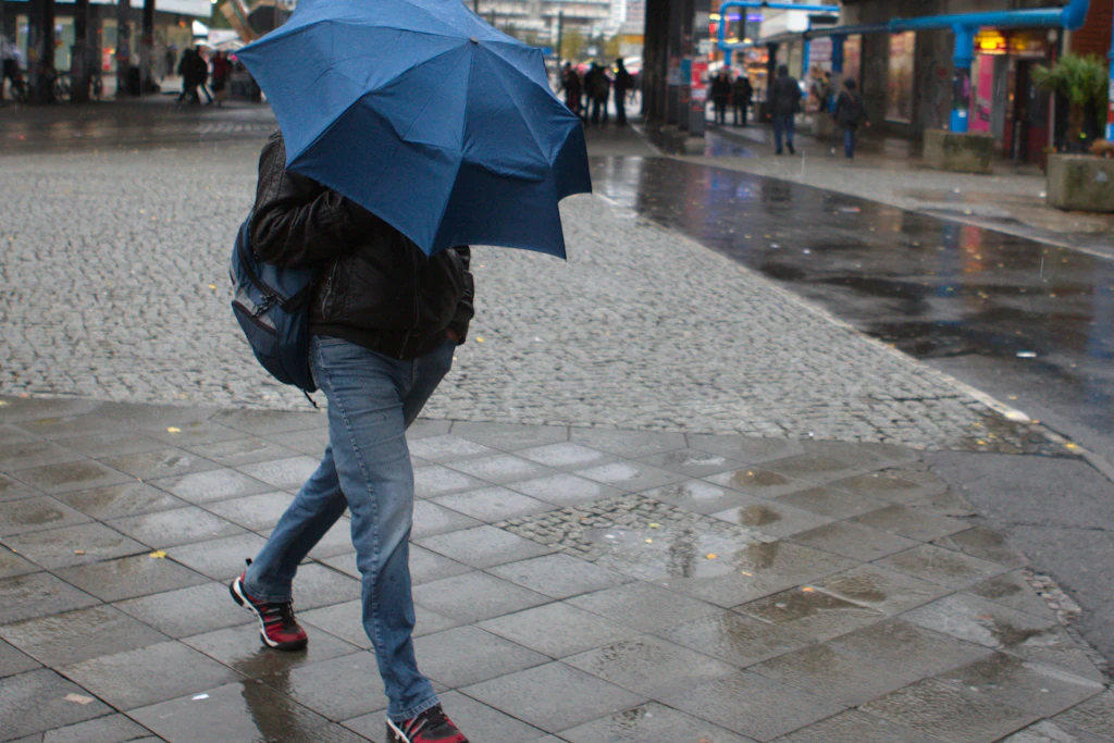 Ein Mann kämpft in Berlin auf dem Alexanderplatz mit seinem Regenschirm gegen den Wind.