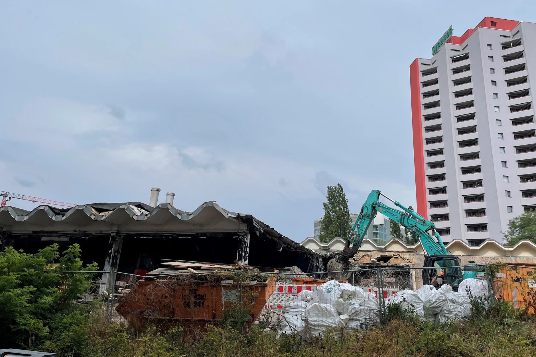 Bagger tragen die Betonteile der Schwimmhalle in der Holzmarktstraße ab. Das markante Wellendach steht noch.