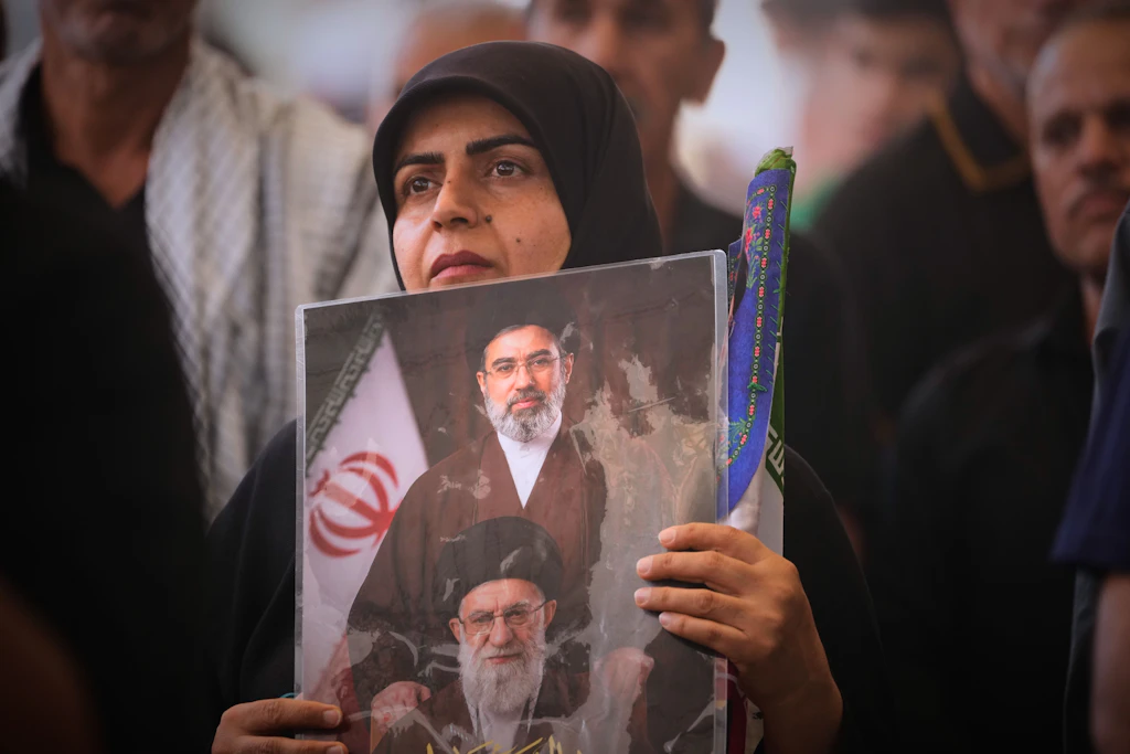 Eine Trauernde hält während eines Trauerzuges für den älteren Chamenei im Imam-Ali-Schrein in Nadschaf ein Porträt hoch, das den obersten Führer des Iran, Mojtaba Chamenei (oben), und dessen verstorbenen Vater, Ajatollah Ali Chamenei, zeigt.