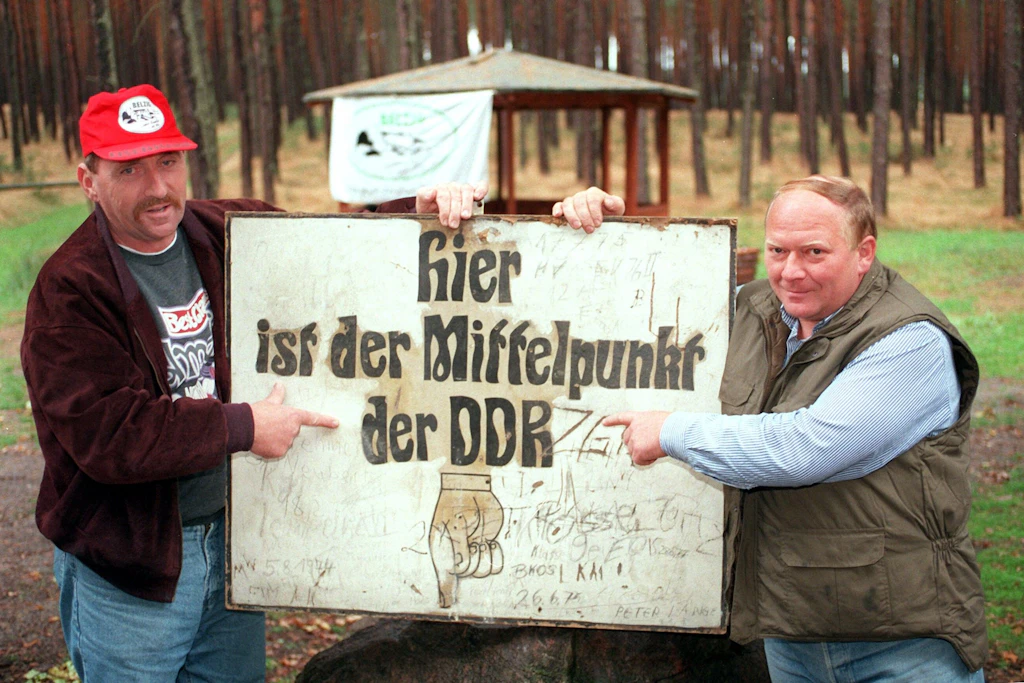 Klaus Nichelmann (l) und Bernd Schulze vom Verein Pro Belzig mit dem originalen Schild zur Kennzeichnung des Mittelpunkts der DDR. Ihr „Belziger Mittelpunkt-Kräuter“, ein „32-prozentiger Halbbitterlikör für Ossis und Wessis“, hat die Marktreife dann doch nicht erreicht.