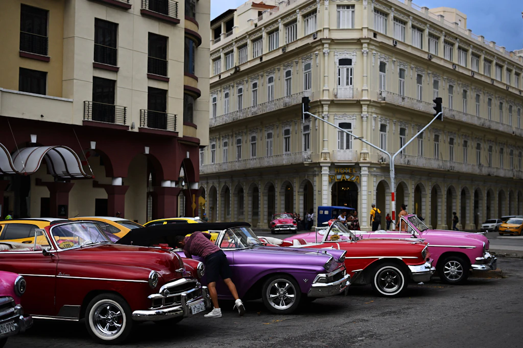 Oldtimer-Fahrer warten vor dem Hotel Plaza in Havanna auf Touristen.