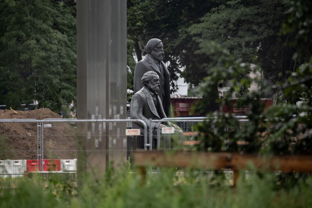 Marx und Engels warten im Regen zwischen Bauschutt, hier am 14. Juli 2026.