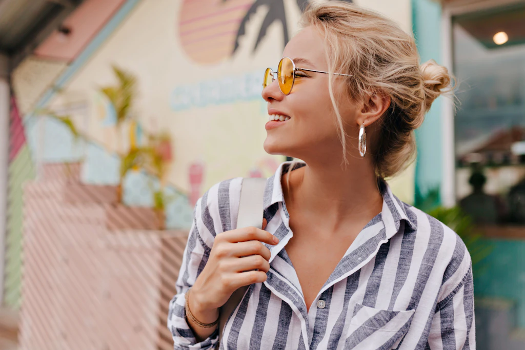 Mit Sonnenbrille und einem Lächeln startet eine junge Frau leicht und selbstbewusst in die neue Woche.