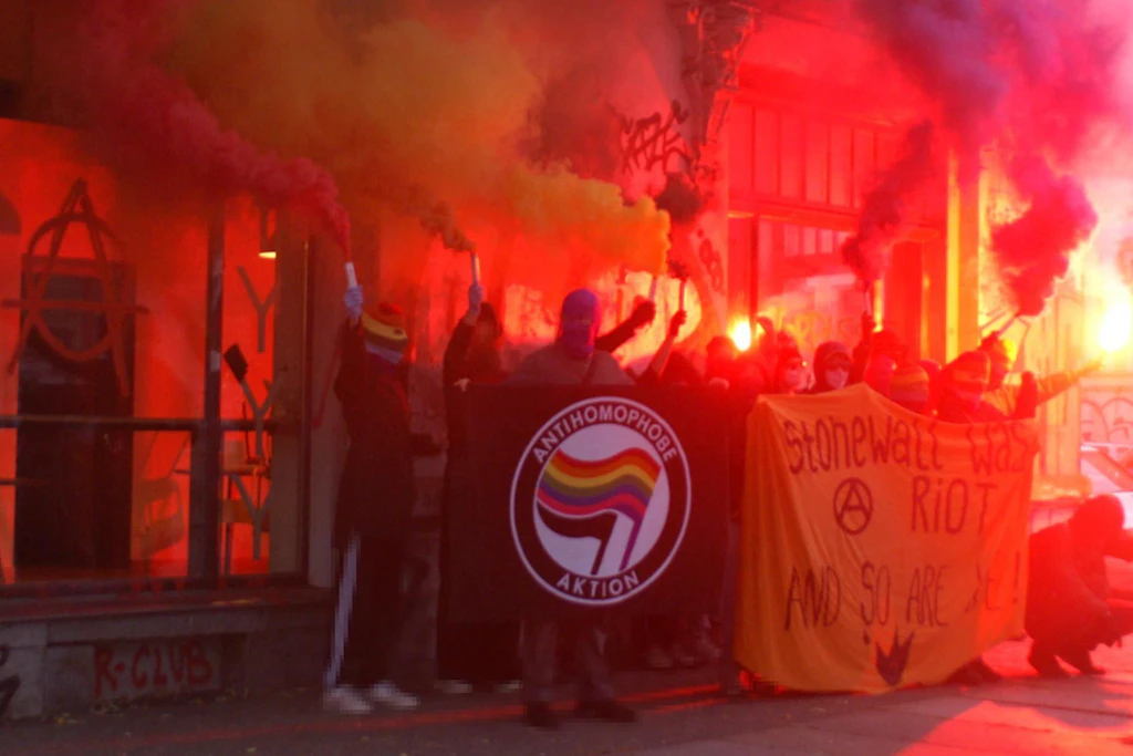 Mit Pyrotechnik posieren die Linksextremen vor dem Café. „Antihomophobe Aktion“ steht auf ihrem Banner geschrieben. Es ist der Fahne der Antifa nachempfunden.