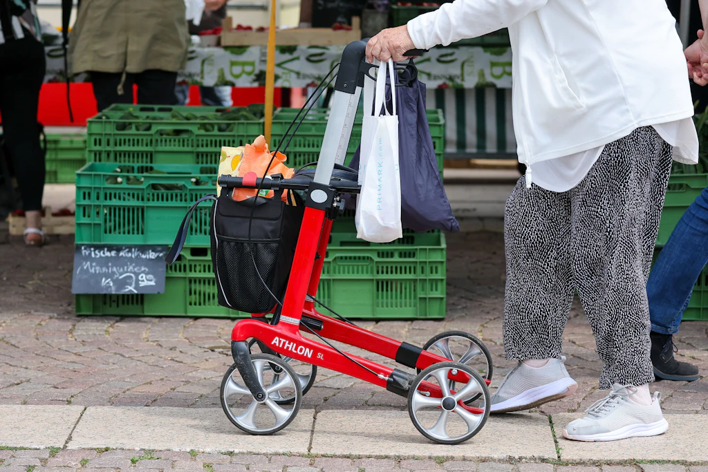 Eine Seniorin geht mit ihrem Rollator über einen Wochenmarkt.