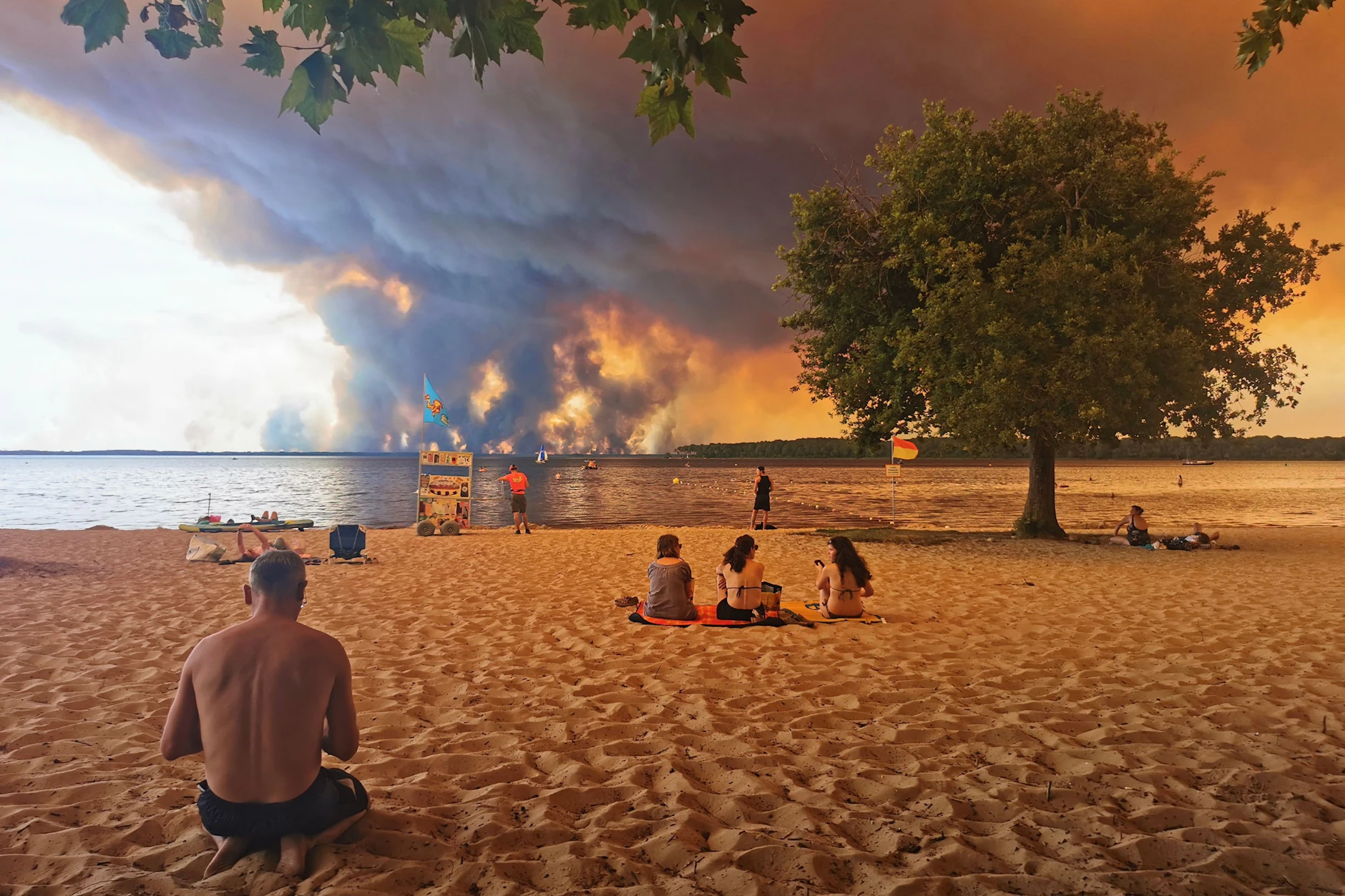 Urlauber sitzen am Strand von Moutchic in Lacanau im Südwesten Frankreichs, während Rauchwolken von einem Waldbrand in den Himmel aufsteigen.