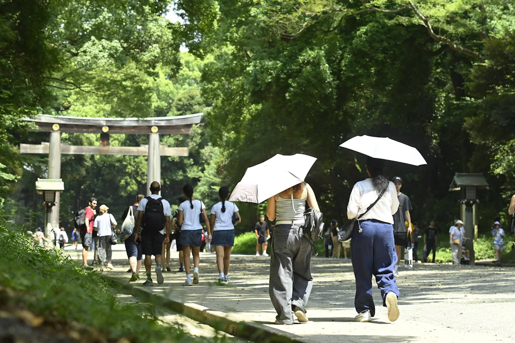 Besucher schützen sich auf dem Gelände des Meiji-Schreins in Tokio mit Sonnenschirmen vor der Hitze.