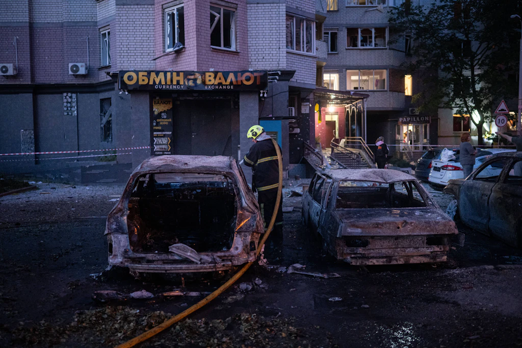 Ein Feuerwehrmann zwischen ausgebrannten Autos vor einem bei russischen Raketenangriffen beschädigten Wohnhaus in Kiew.