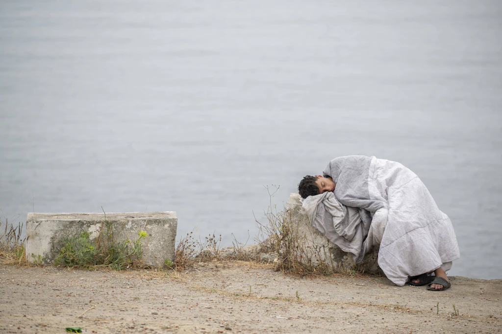 Ein erschöpfter Migrant ruht in eine Decke gehüllt an der Küste von Ceuta.