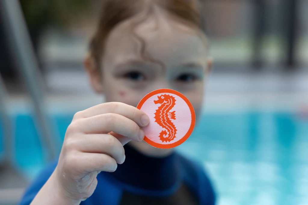 Ein sechsjähriges Kind zeigt sein Seepferdchen-Abzeichen. Darauf kann es zu Recht stolz sein – doch das heißt nicht, dass das Kind sicher schwimmen kann.