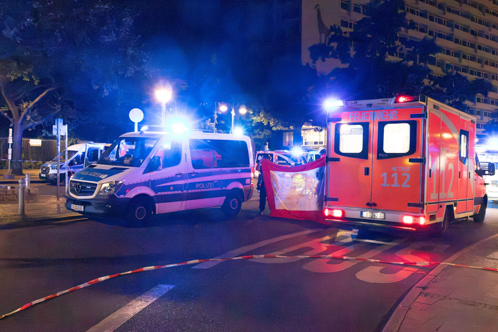 Zwischen Polizeifahrzeug und Rettungswagen der Berliner Feuerwehr halten Einsatzkräfte in der Nacht einen Sichtschutz am Hardenbergplatz.