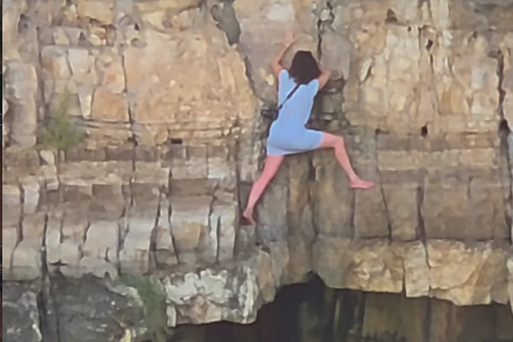 Eine Touristin klettert an einer Felswand in Polignano a Mare hoch und kommt dann weder vor noch zurück.