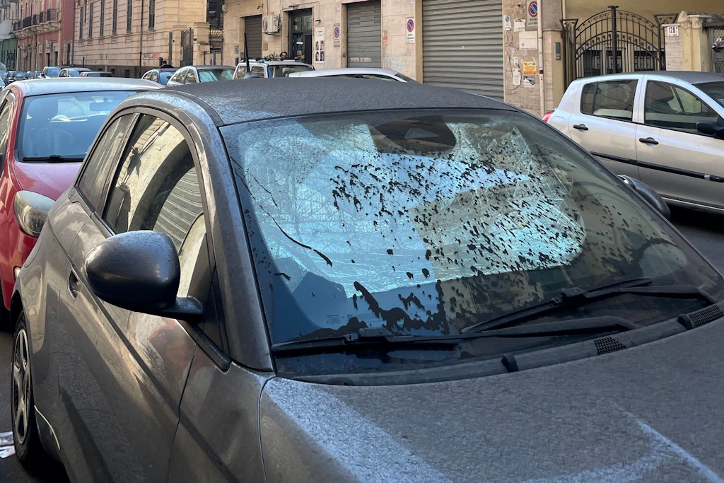 Feiner Ätna-Staub bedeckt Dach, Motorhaube und Scheibe eines geparkten Autos in Catania.