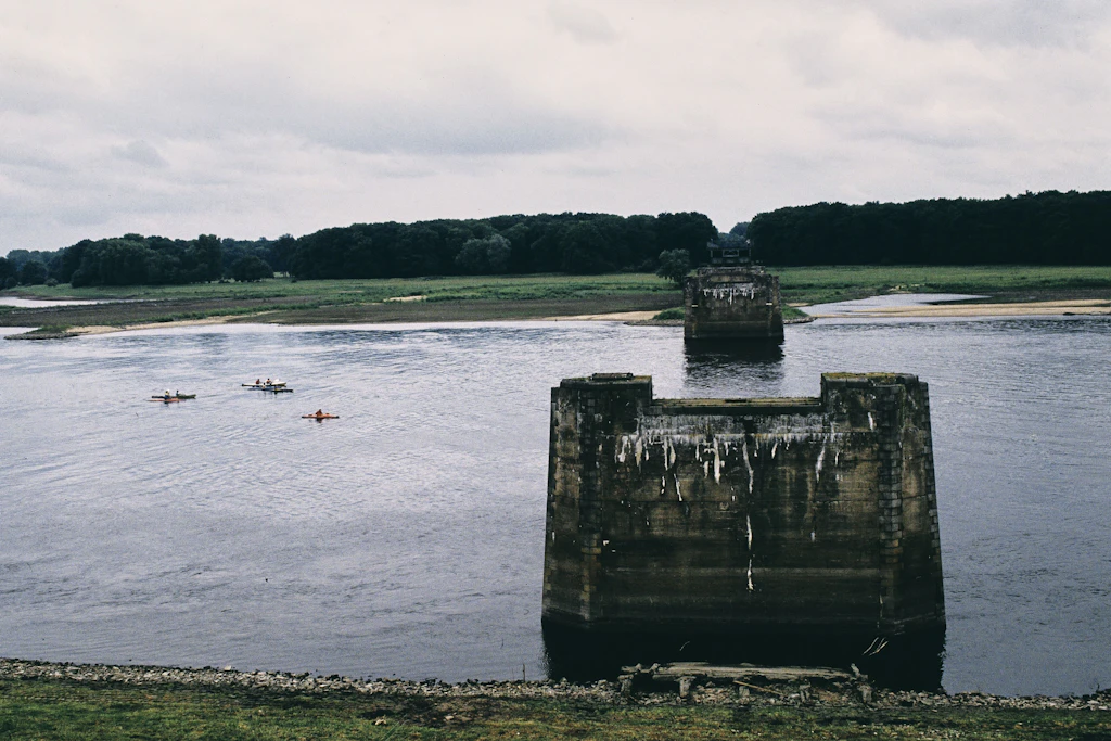 Kanuten fahren auf der Elbe an einer gesprengten Eisenbahnbrücke vorbei. Das jenseitige Ufer war DDR-Gebiet. 1984 von Niedersachsen aus gesehen.