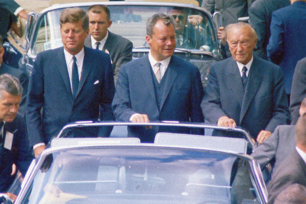 West-Berlin 1963. US-Präsident John F. Kennedy besucht die Mauerstadt. Im offenen Wagen fährt er durch die City. Neben ihm der Regierende Bürgermeister Willy Brandt und der deutsche Kanzler Konrad Adenauer (v. li.).