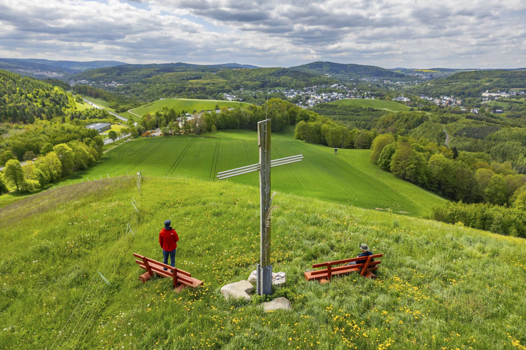 Wanderer unter dem Pilger-Kreuz des Jakobsweges Silberberg mit Blick über die Landschaft bei Bad Schlema: In Sachsen werden Tourismustreiber wie das Erzgebirge, das Vogtland oder die Sächsische Schweiz&nbsp; besonders gefördert.