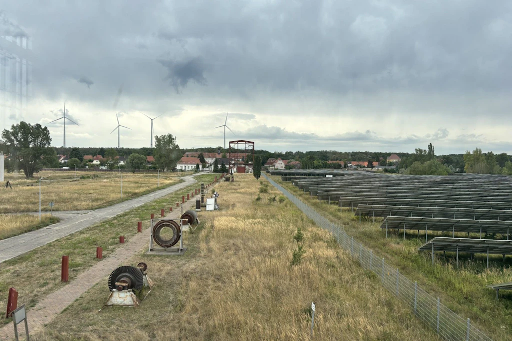 Blick über das Kraftwerksgelände. Rechts die Photovoltaikanlage, hinten Windräder.