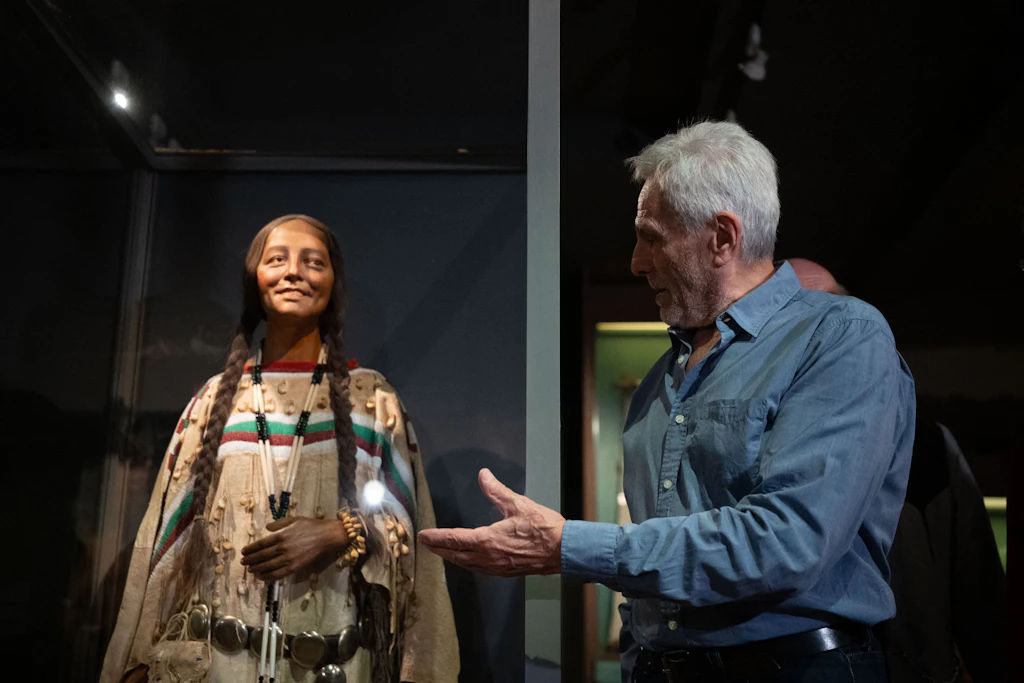 Schauspieler Gojko Mitić steht bei der Enthüllung der Kostümfigur einer Blackfoot-Frau neben der Vitrine im Karl-May-Museum.