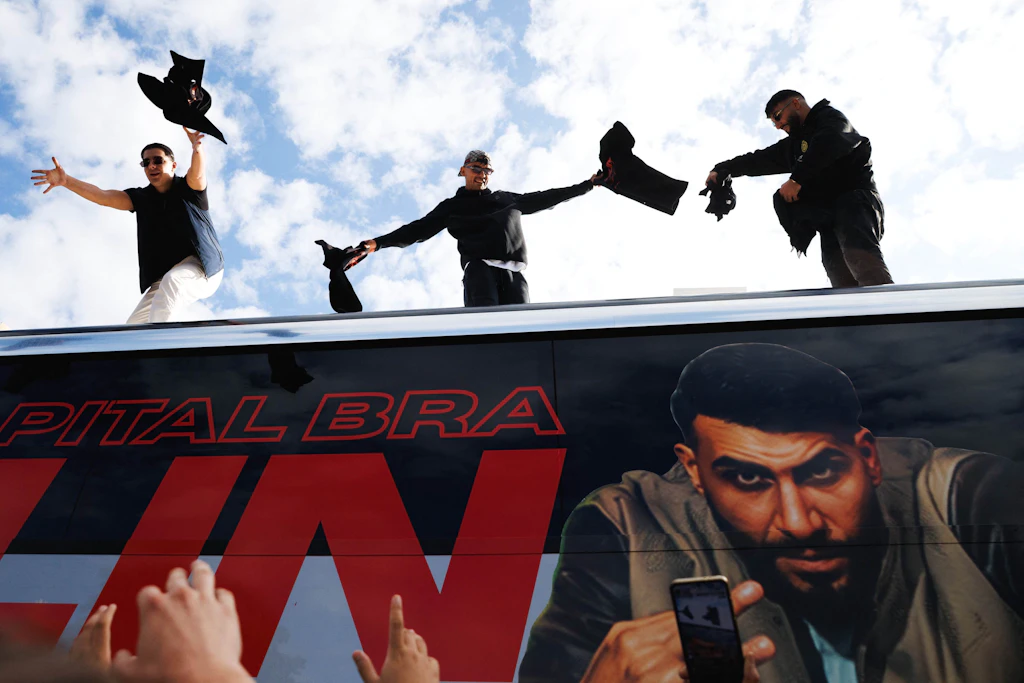 Die Rapper Lacazette (l.), Capital Bra (M.) und Samra (r.) werfen bei einer spontanen Fan-Aktion am Oranienplatz im Berliner Stadtteil Kreuzberg T-Shirts von einem Tourbus.