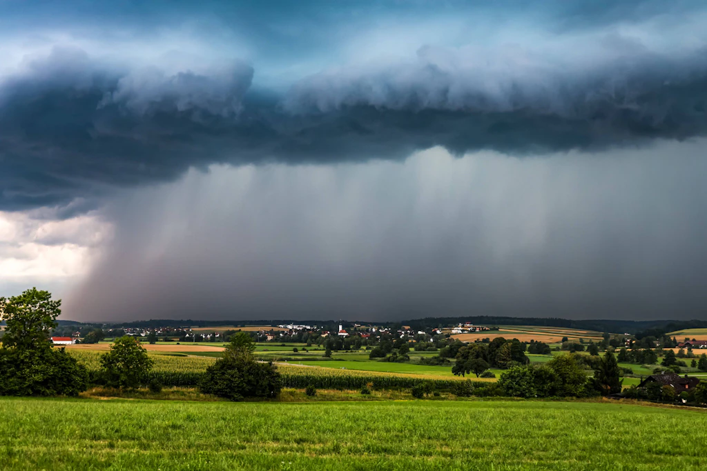 Eine Gewitterfront zieht mit sichtbaren Regenschleiern über eine Ortschaft: Am Donnerstagabend erreichen die ersten starken Gewitter den Westen Deutschlands. (Symbolbild)