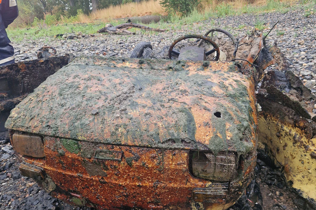 Die Überreste eines alten Kleinwagens liegen nach der Bergung aus dem Rhein auf dem Trockenen.