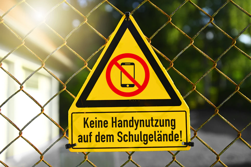 Ein gelbes Verbotsschild am Zaun einer deutschen Schule – in Frankreich soll dieses Verbot ab September auch für die 15- bis 18-Jährigen gelten (Symbolfoto).