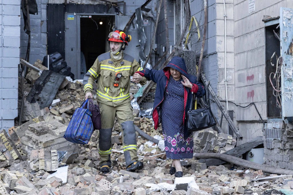 Ein Feuerwehrmann bringt eine Frau nach einem russischen Raketenangriff auf ein Wohnhaus im Kiewer Stadtteil Solomjanka in Sicherheit.