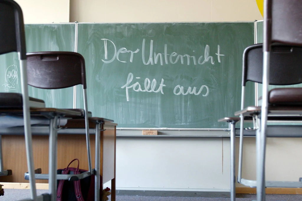 Symbolbild Bildungskrise: Ein verlassenes Klassenzimmer – „Der Unterricht fällt aus" steht auf der Tafel. Während der Staat sich zurückzieht, drängen private Akteure in die Lücke