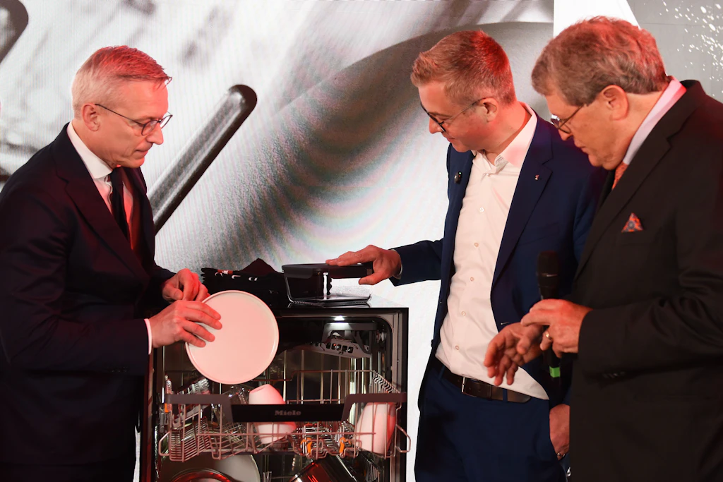 Politiker räumen zusammen mit dem Miele-CEO Teller in einen neuen Geschirrspüler ein.