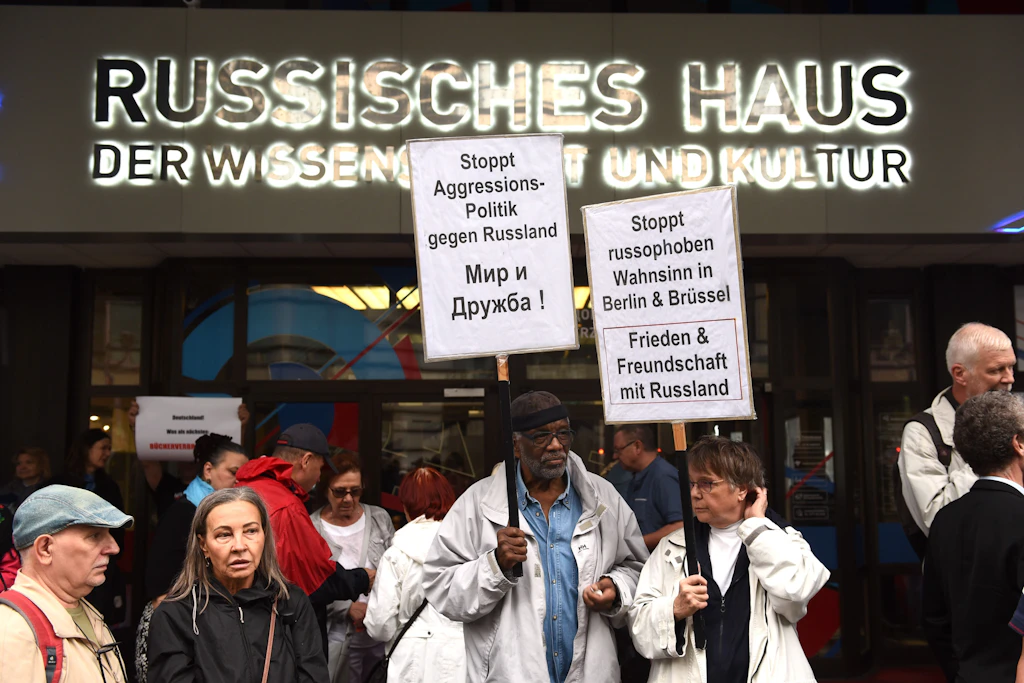 Teilnehmer der BSW-Kundgebung mit Schildern vor dem Eingang des Russischen Hauses.