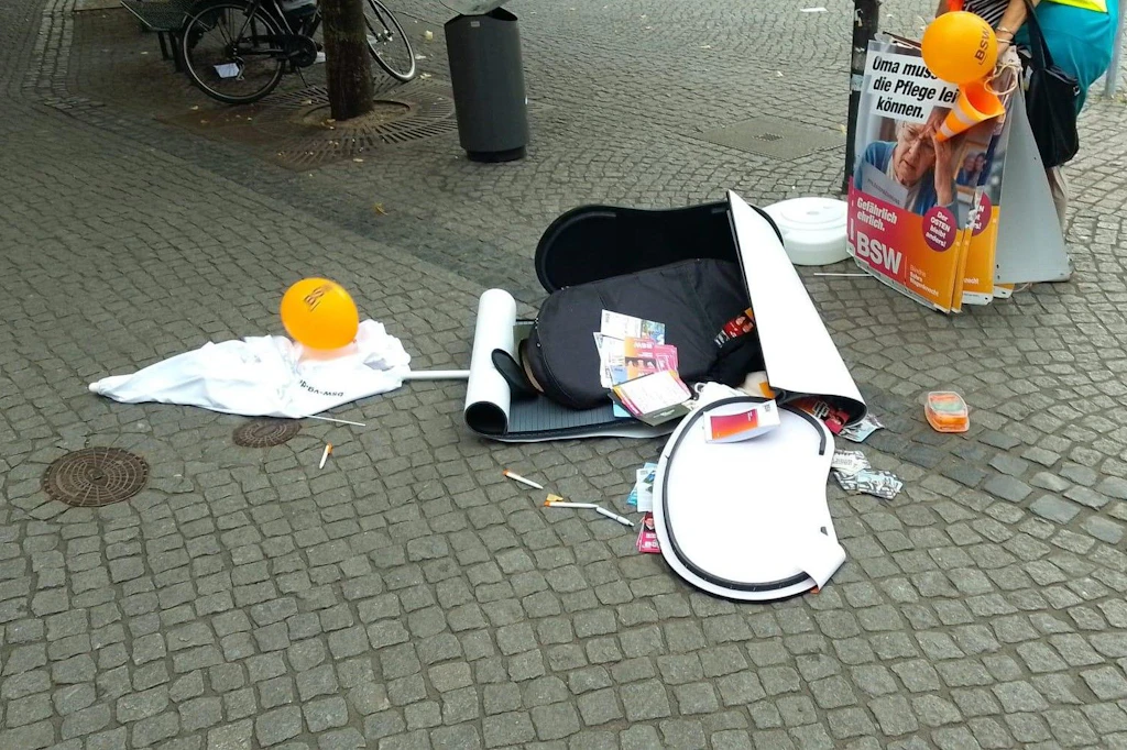 Ein zerstörter BSW-Wahlstand am Hasselbachplatz in Magdeburg. Auf dem Pflaster liegen umgeworfene Aufsteller, Plakate, Flyer und orangefarbene BSW-Luftballons verstreut.