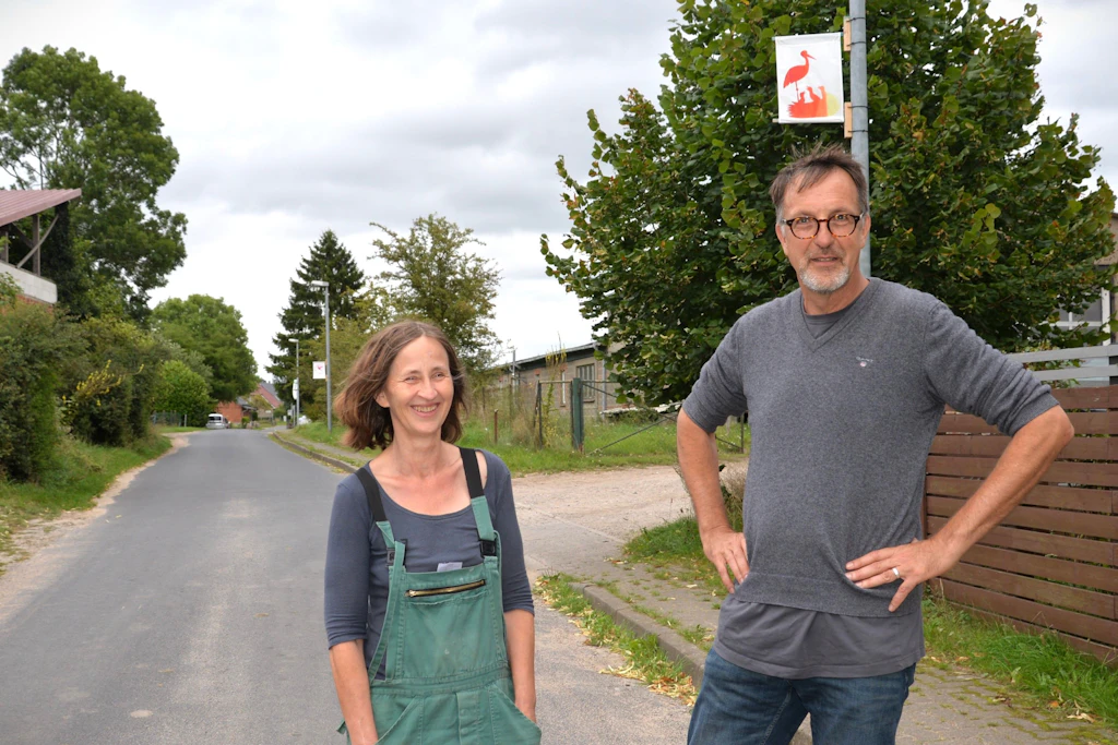 Auf einer Dorfstraße in Qualitz: Sabine Adolphi und Andreas May vom Vorstand des Kunstvereins Allerhand e.V. unter dem Siebdruckbanner mit den Störchen vom Grundstück nebenan.
