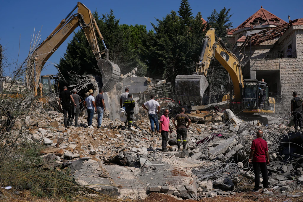 Menschen beobachten, wie Rettungskräfte mit Baggern nach Opfern unter den Trümmern eines Gebäudes suchen, das bei einem israelischen Luftangriff im südlichen Dorf Kfar Rumman im Libanon zerstört wurde.