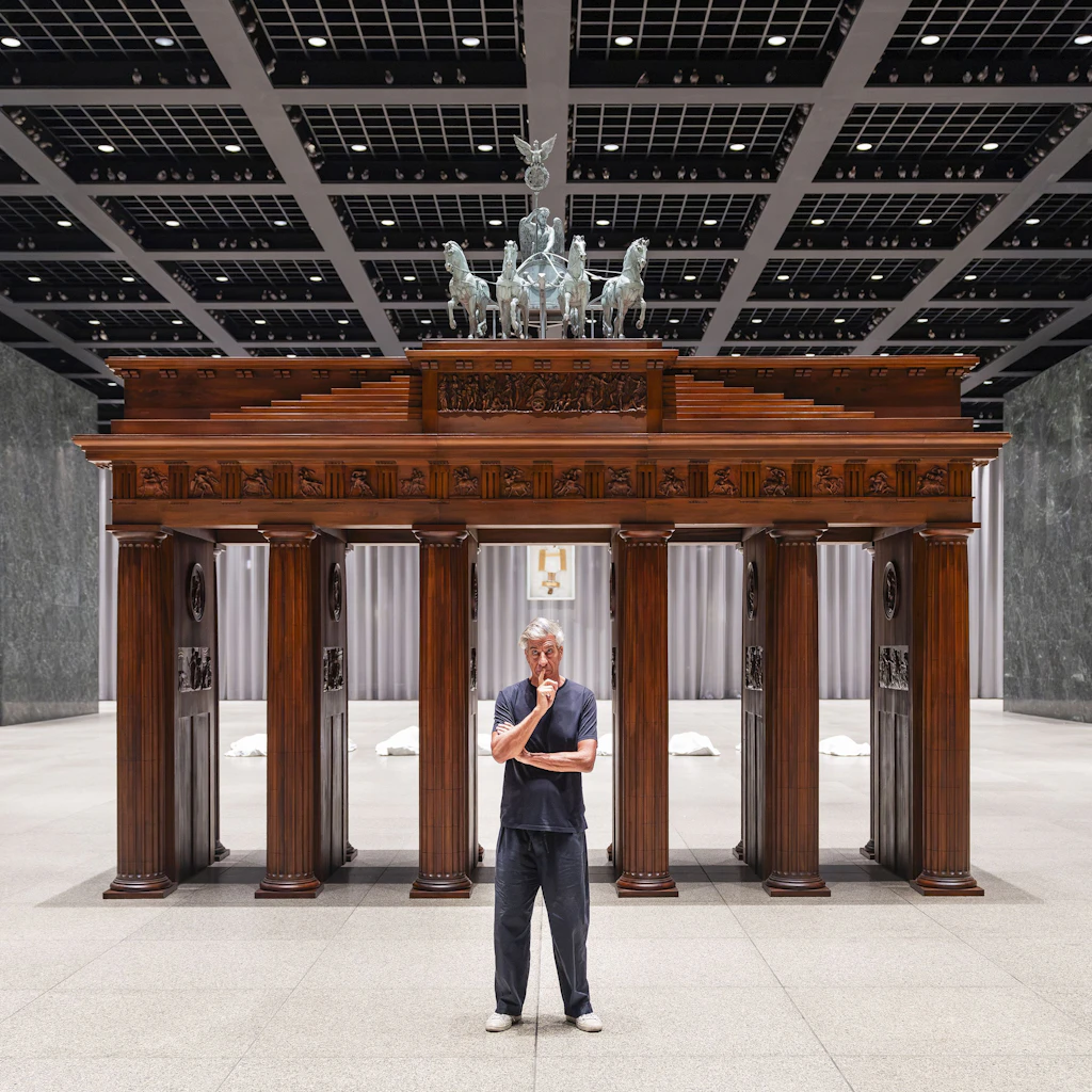Cattelan vor seinem nachgebildeten Brandenburger Tor: Das deutsche Heiligtum setzt er durch den Bezug zu Dantes „Inferno“ ins fiktive Fegefeuer. Hinten liegen die toten Opfer der Geschichte, gemeißelt aus Carrara-Marmor.