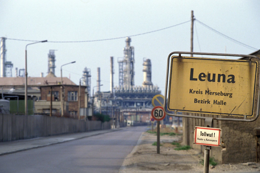 Im April 1990: Das Ortsschild von Leuna mit Blick auf das Gelände des VEB Leuna-Werke in Sachsen-Anhalt.