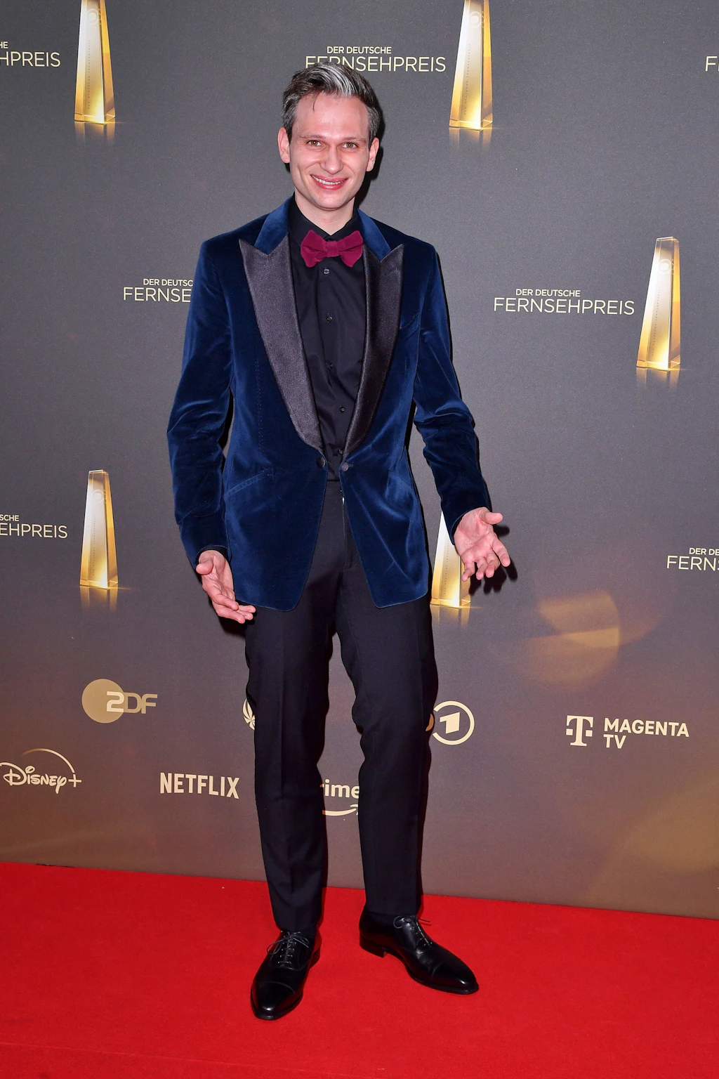 Flop: Fabian Köster ist bekannt für seine Satire und bissigen Kommentare. Da wird er uns wohl auch einen spitzen Kommentar zu seiner fragwürdigen Garderobe erlauben. An diesem Abend setzt der Komiker auf ein schwarzes Hemd mit passender Anzughose und kombiniert dazu ein tiefblaues Samtsakko mit schwarzem, satiniertem Revers. Die Materialwahl erweist sich dabei als erster Fehlgriff: Der Samt wirkt hier nicht edel, sondern altbacken. Die Kombination aus Dunkelblau und Schwarz lässt uns wiederum erneut an die alte Stilregel glauben, dass die beiden Farben grundsätzlich nicht zusammenpassen. Die rote Fliege ist schließlich – offensichtlich im schlechtesten Sinne – die Kirsche auf der Sahnetorte.