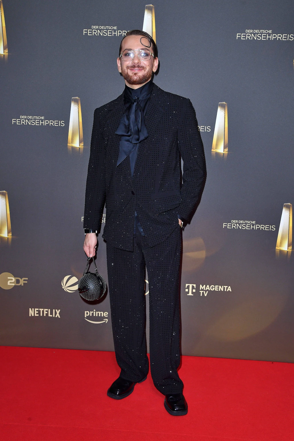 <strong>Top: Riccardo Simonetti</strong> hätte an diesem Abend eigentlich einen Preis für seltene modische Stilsicherheit verdient. Und das, obwohl seine Outfitwahl ganz ohne dramatisches Volumen oder knallige Farben auskommt. Sein lässig geschnittener Anzug von Karl Lagerfeld ist mit dunklen Glitzersteinen besetzt, die subtil schimmern. Dazu kombiniert er eine satinierte Schluppenbluse mit locker gebundener Schleife und eine Brille mit metallischem Gestell. Wir finden: Damit spendiert er uns eine wohltuende Ruhepause für die Augen.