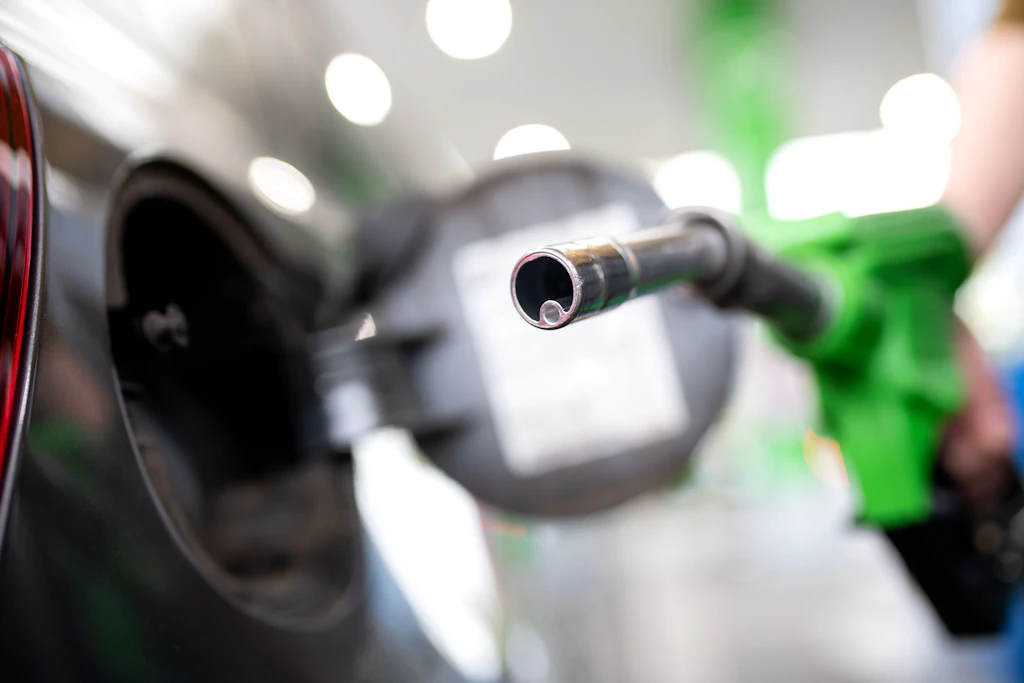 Eine Frau hält an einer Tankstelle an einer Zapfsäule eine Zapfpistole in der Hand.